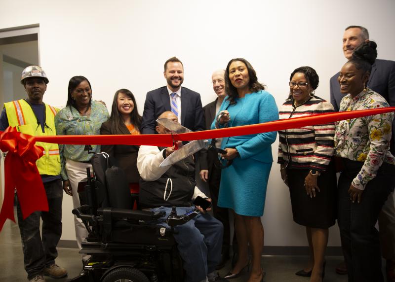 A multi-racial group including Mayor London Breed cut a bright red ribbon