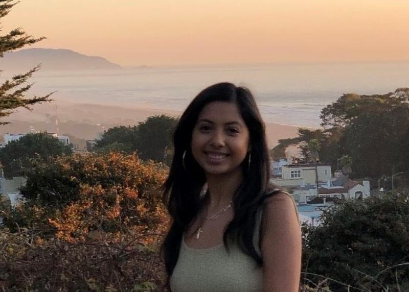 A latinx young woman stands in front of a sunset 