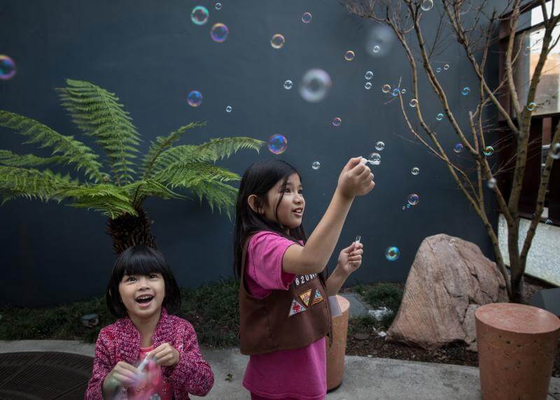 Two asian-american sisters blow bubbles in a courtyard