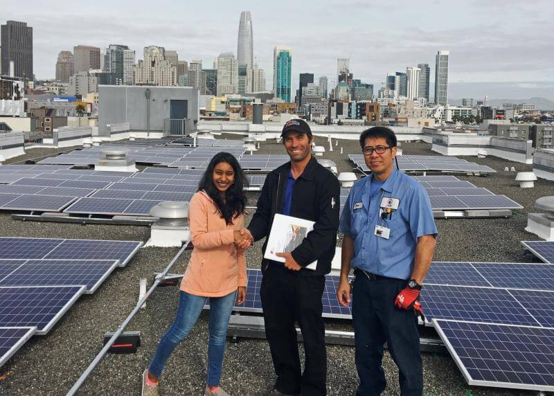 multi-racial group stands in front of rooftop solar panels
