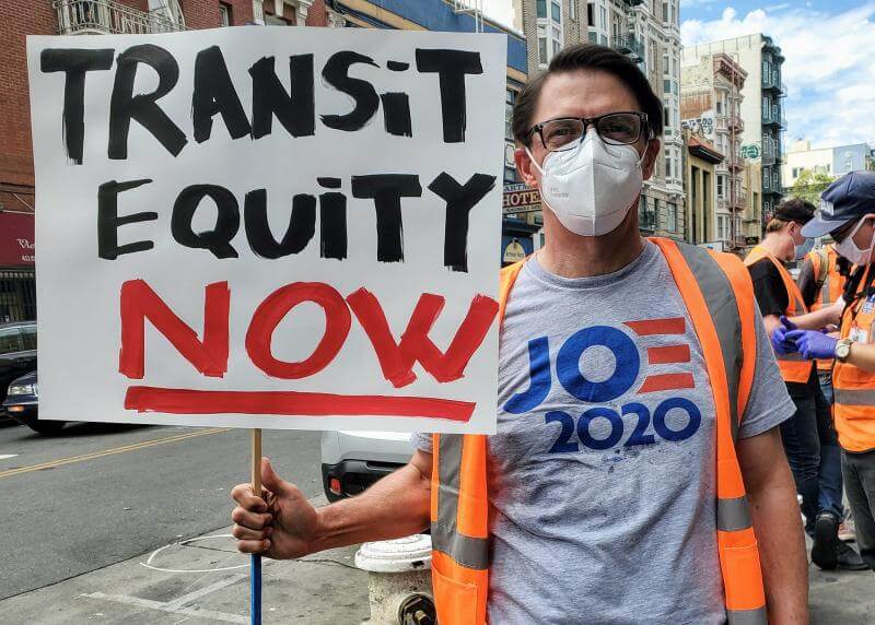 A TL Activist holds up a sign reading "Transit Equity Now"