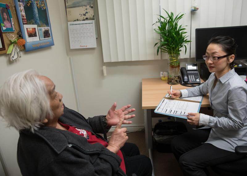 An Asian social worker assists an Asian senior at a desk 