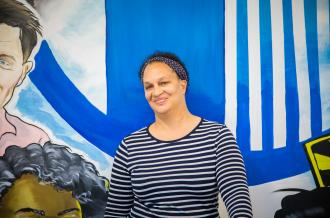 A woman stands against a mural and smiles at the camera