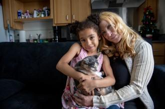 A young black girl and her white mom sit together on a couch cradling a kitten