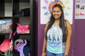 A young Indian woman stands near backpacks smiling