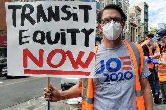 A TL Activist holds up a sign reading "Transit Equity Now"