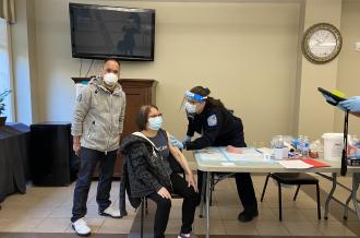 A senior tenant gets a shot from a medical professional, a social worker stands by