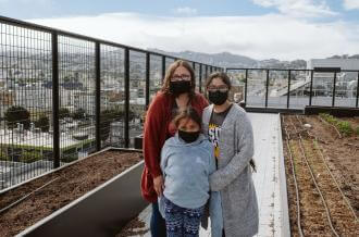 A mother and her two daughters stand on the rooftop of Casa Adelante -2828 16th Street