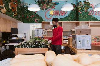 A Black staff member sorts bok choy with a colorful mural in the background