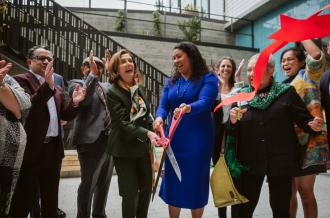 A diverse group including Speaker Pelosi and Mayor Breed cheer at a ribbon-cutting