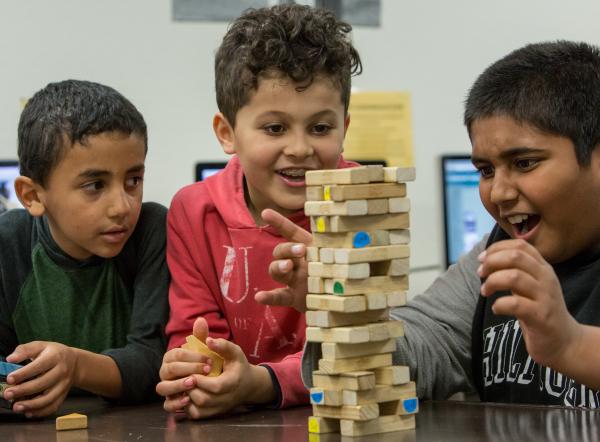 A multi-racial group of young boys excitedly play jenga 