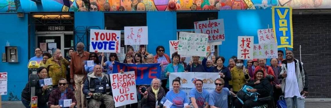 Diverse group of people pose in front of a mural, Many hold signs related to voting